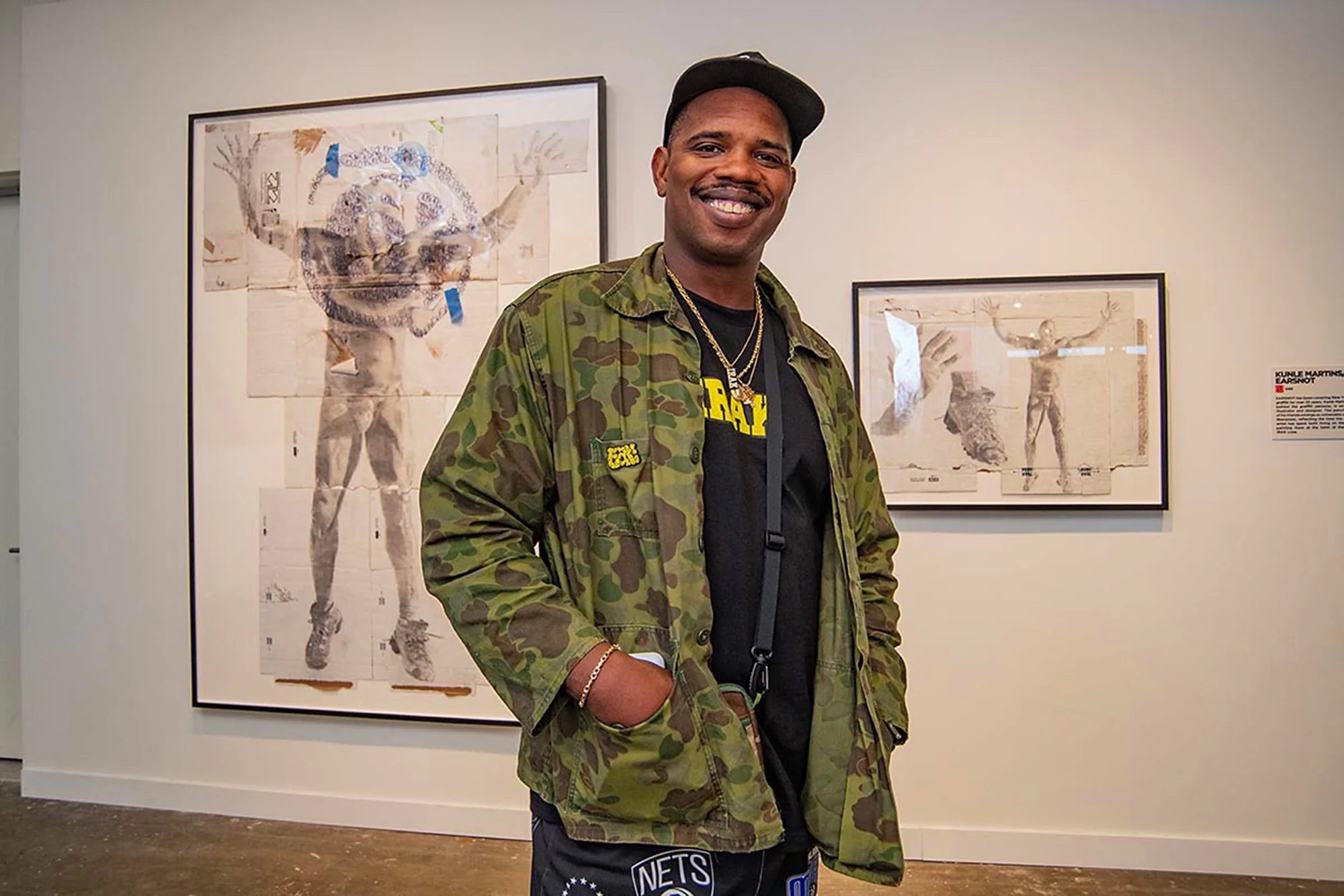 Kunle Martins smiling in front of two framed portrait works at Beyond the Streets New York