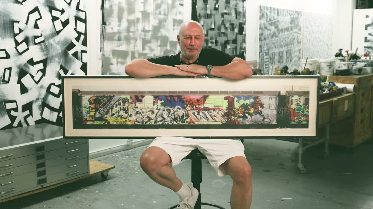 Eric Haze seated behind Henry Chalfant’s panoramic photograph of a graffiti-covered subway car