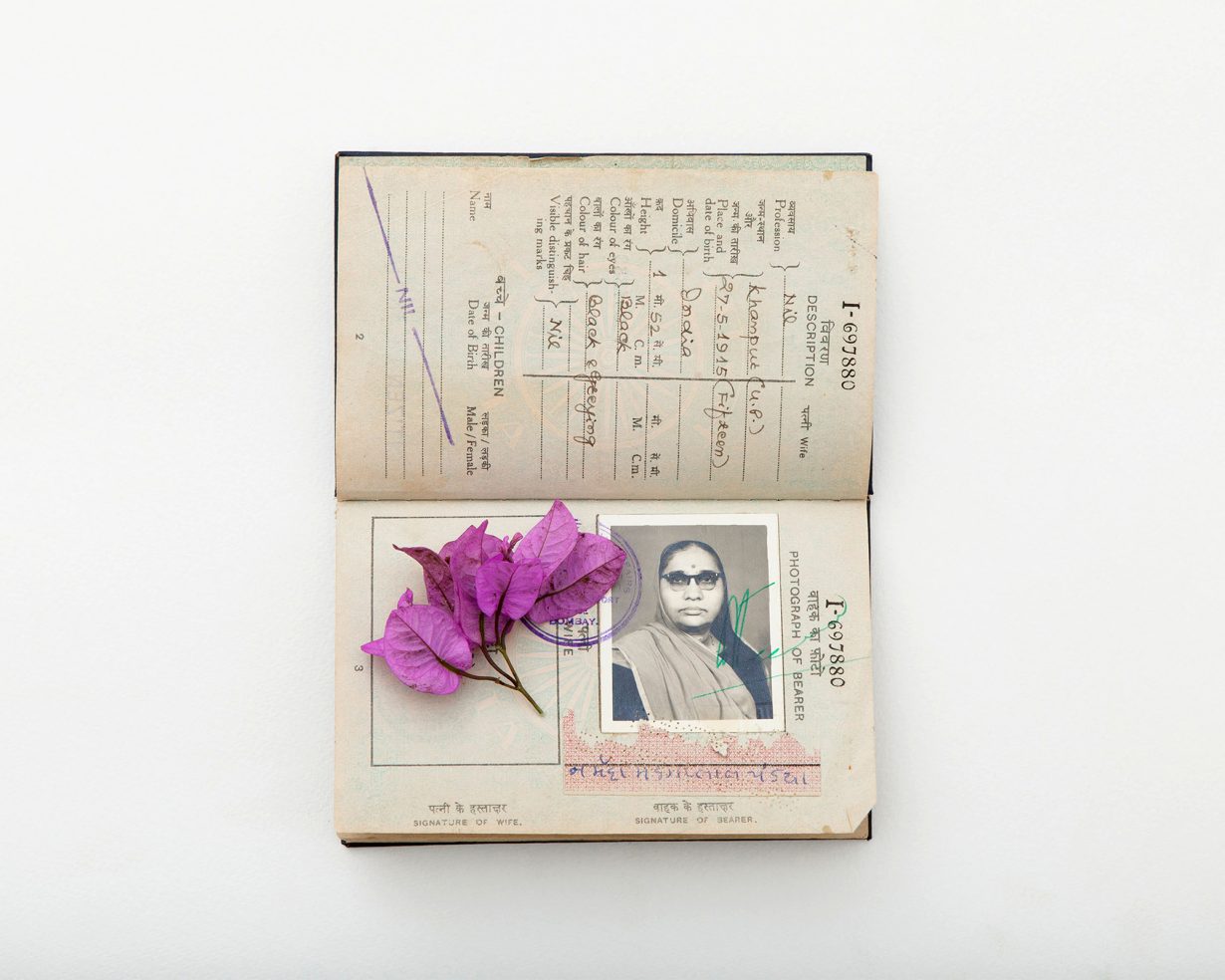 An open Indian passport containing a black-and-white portrait is overlaid with bright bougainvillea flowers