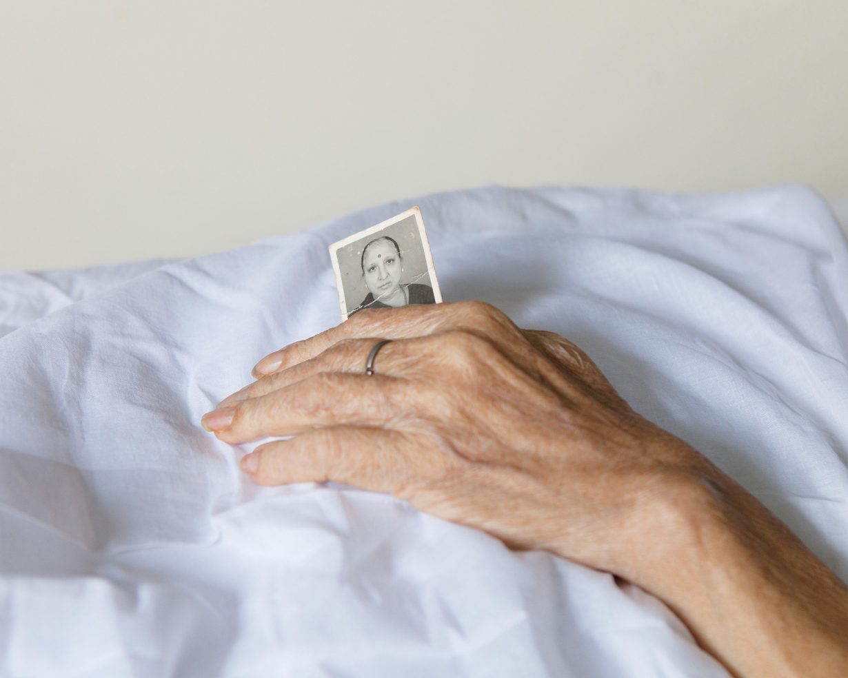 An elderly woman’s hands rest on white fabric while holding a small black-and-white portrait