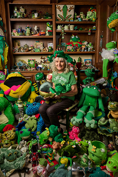 Susan Burgos seated in a room filled from floor to ceiling with frog toys, sculptures, and decorative objects
