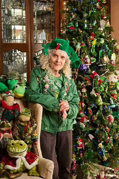 Susan Burgos standing beside a Christmas tree covered in frog ornaments and surrounded by frog figures