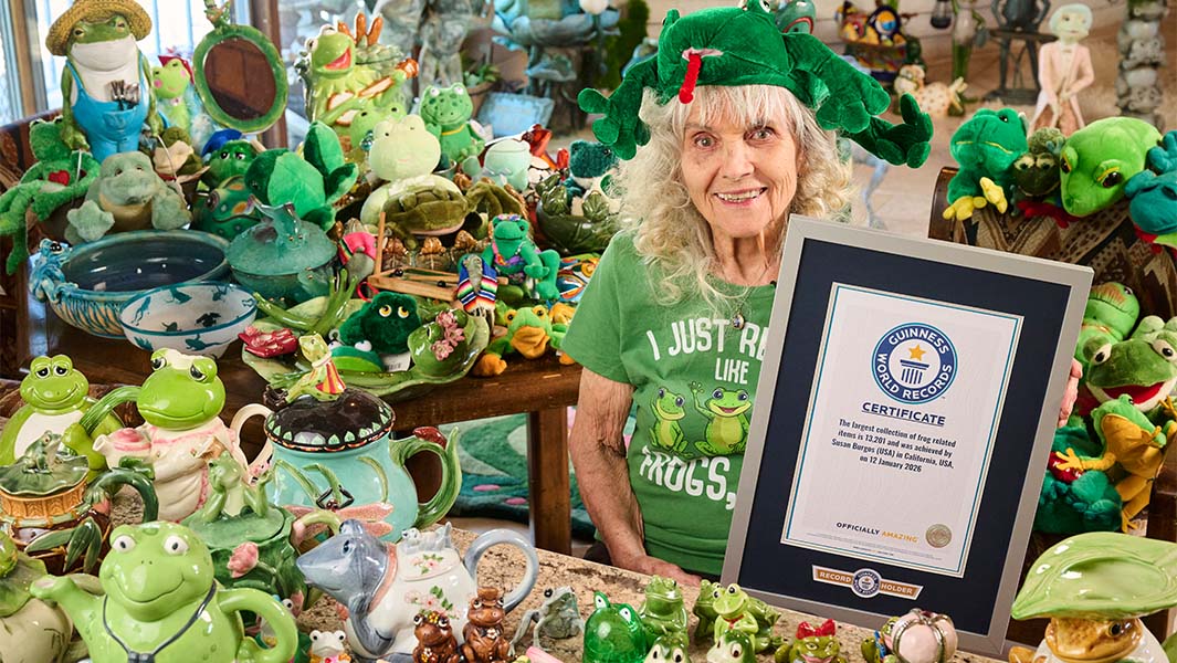 Susan Burgos holds her Guinness World Records certificate amid a table crowded with frog memorabilia