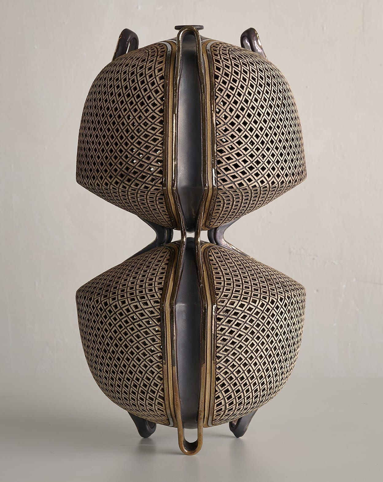 Ibrahim Said’s Delta Vase: two rounded lattice-patterned volumes joined at a narrow waist, with dark vertical bands.