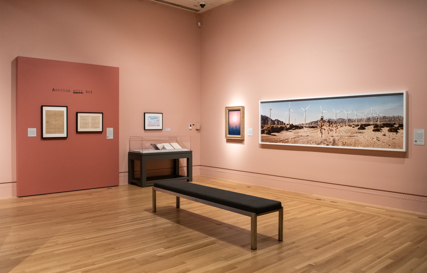 Gallery installation featuring Cara Romero’s panoramic photograph of young men running through the Coachella Valley
