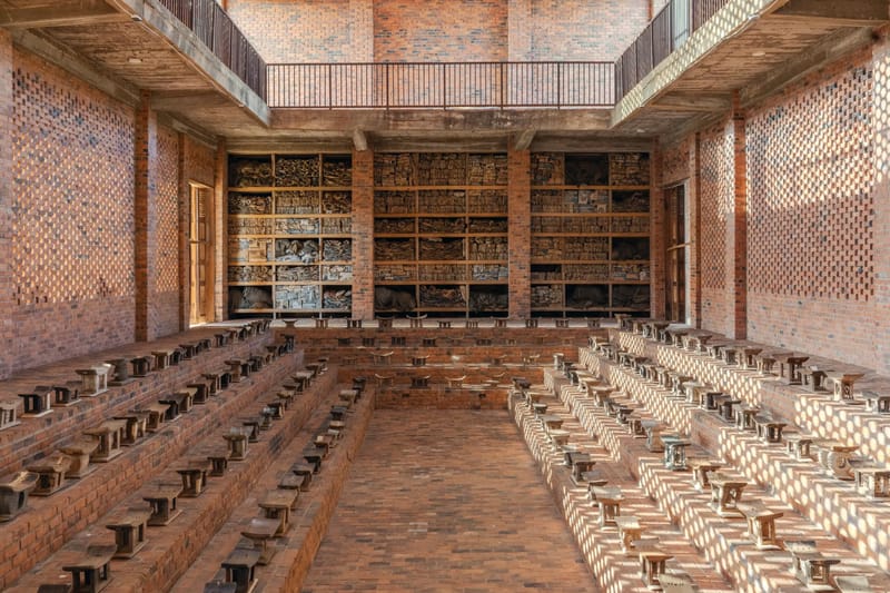 Brick interior at Red Clay in Tamale with rows of small stools and shelves filled with archival materials