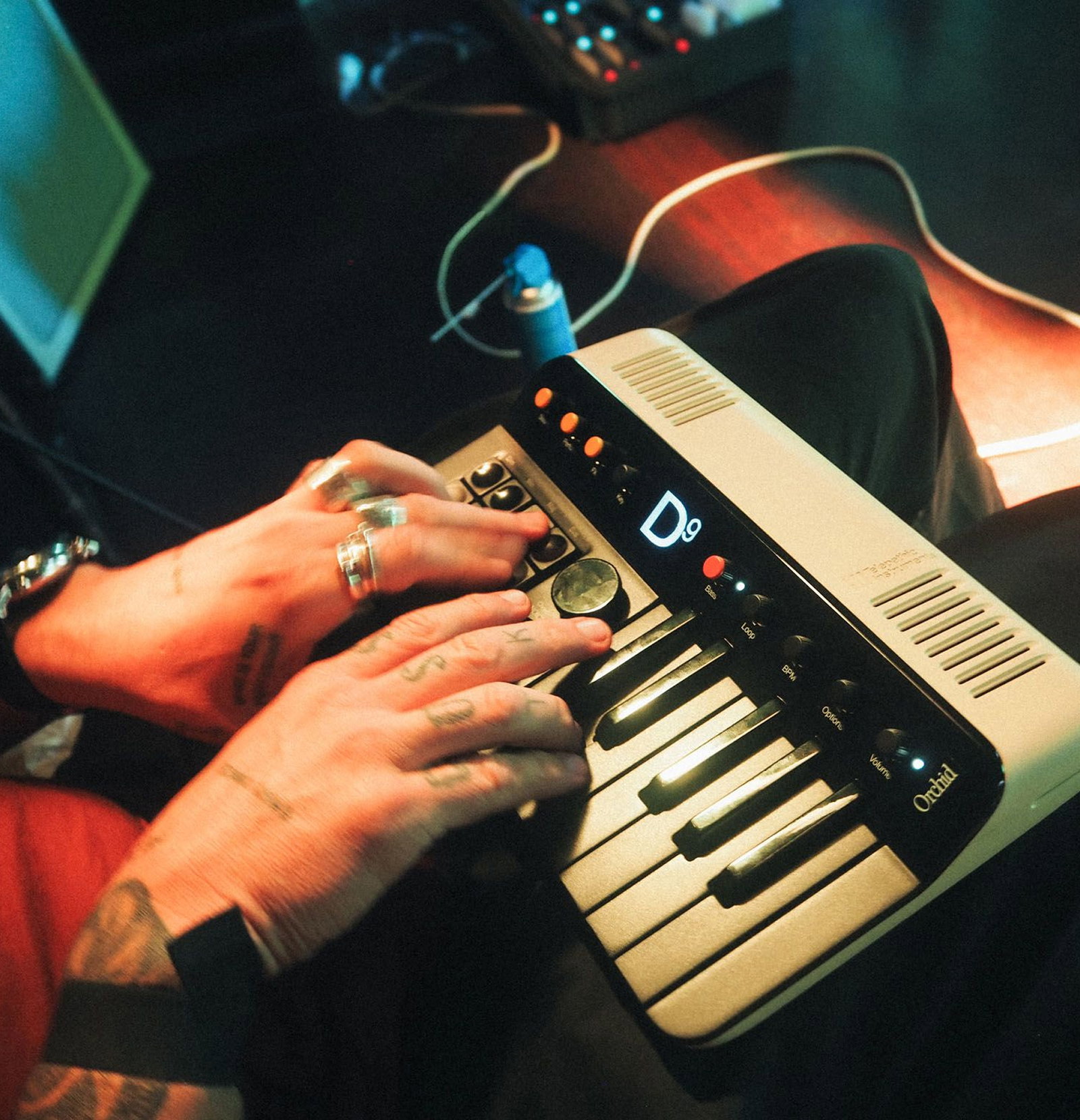 Hands playing a white Orchid synthesizer while its display shows D9 in the custom pixel typeface