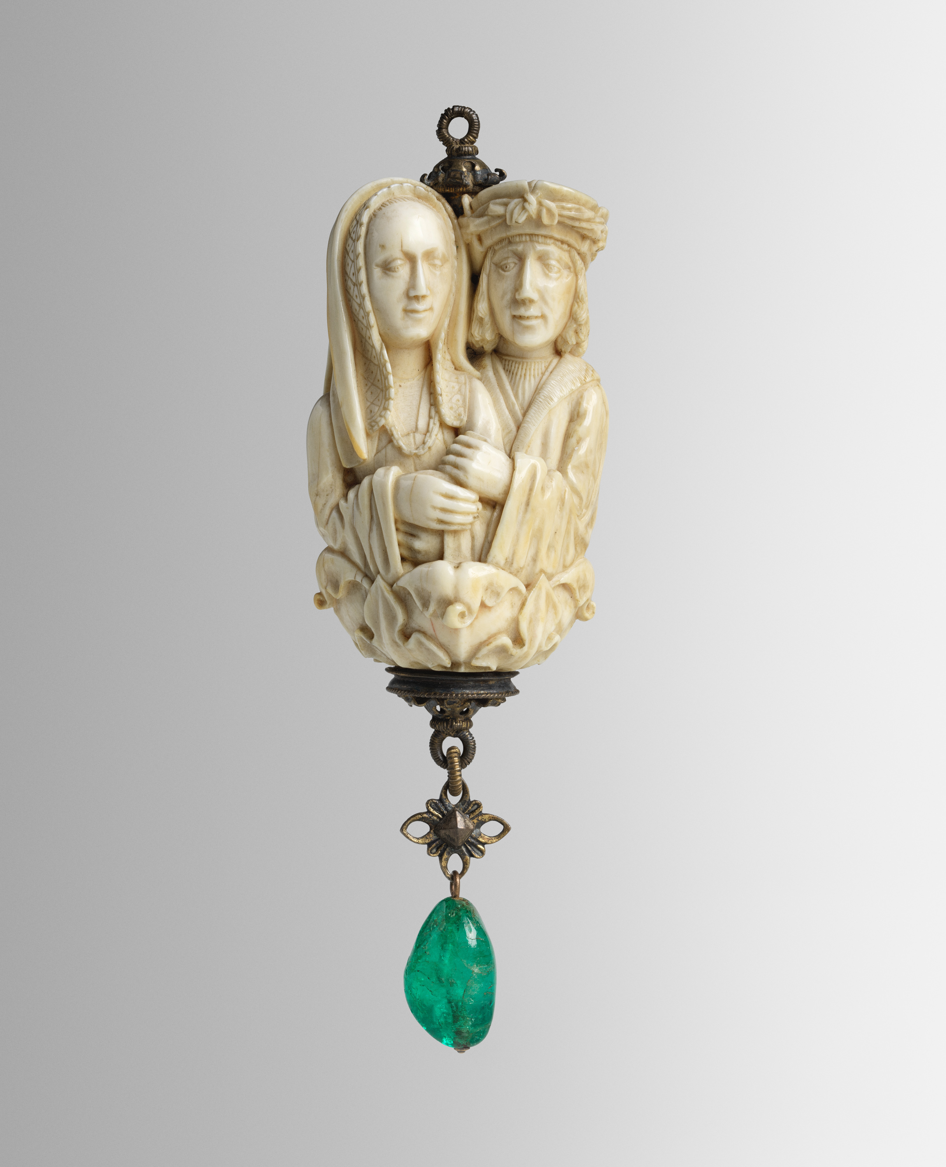 Ivory rosary bead with two lovers above a small skull and a green emerald pendant.