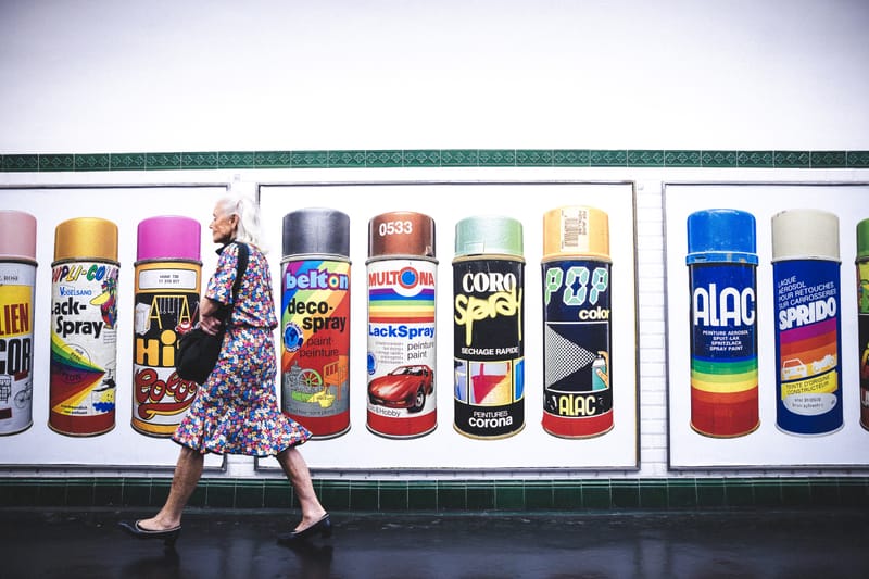 A pedestrian walking past a mural depicting an array of colorful vintage spray-paint cans