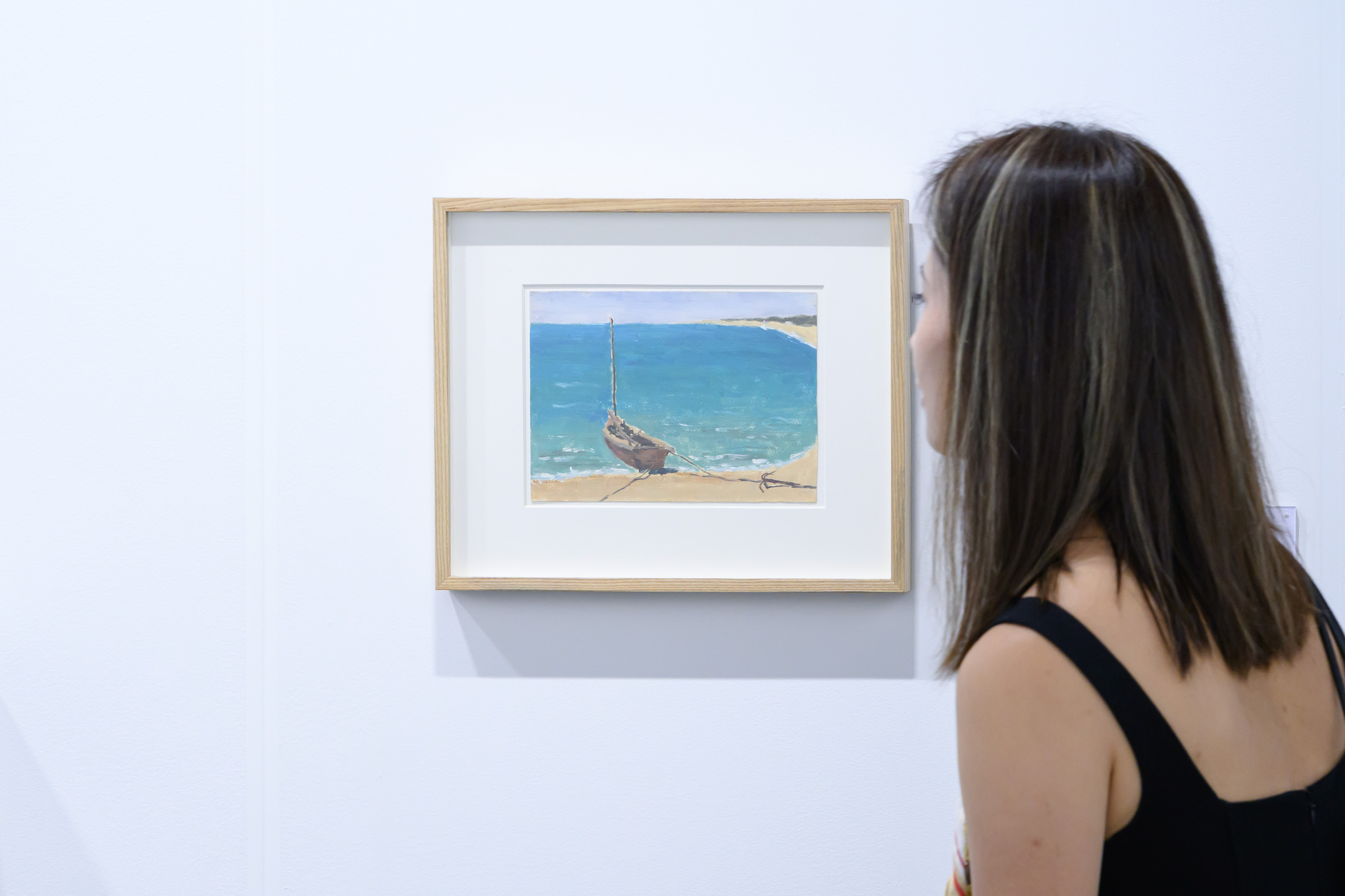 A visitor studying a framed coastal painting at Don Gallery's booth during Art Basel Hong Kong 2026