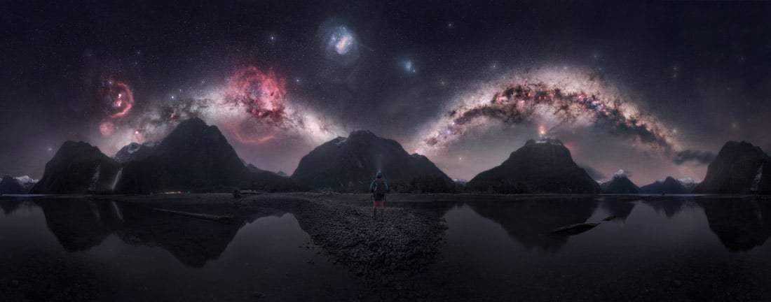 The Milky Way forms two luminous arcs above the mountains and reflective water of Milford Sound
