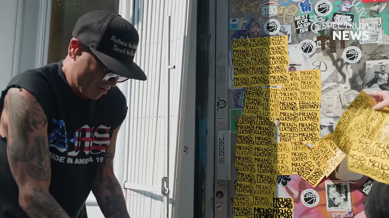 Graffiti writer MQ placing a grid of handwritten yellow stickers on a New York doorway