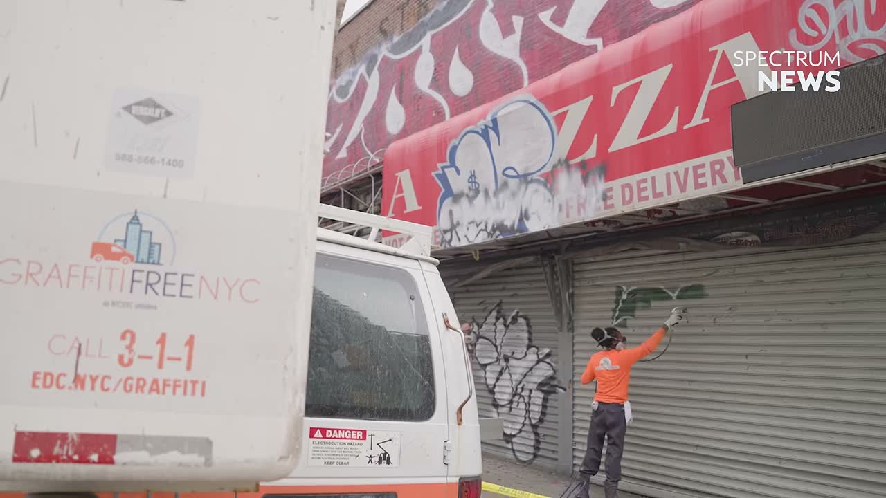A Graffiti-Free NYC worker painting over unauthorized markings on a storefront shutter